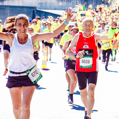 Two white adults running a race with a crowd of many other people
